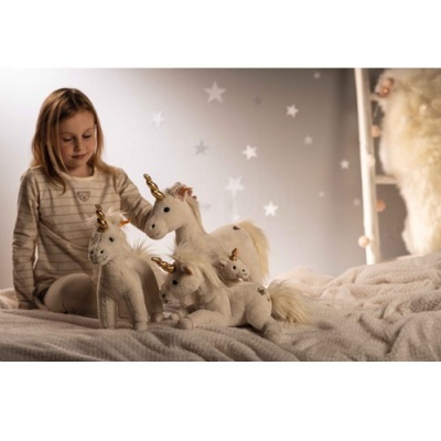 Criança com unicórnios de pelúcia brancos numa cama aconchegante no quarto com paredes cinzentas e estrelas brancas