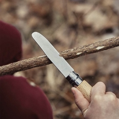 Faca com lâmina metálica e cabo em madeira a cortar ramo seco