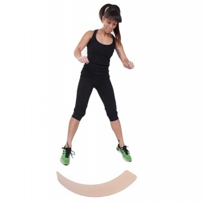 Mulher a saltar sobre plataforma curva cor pele, veste roupa desportiva preta e sapatilhas verdes