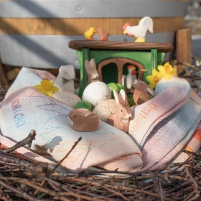 Ninho decorativo com ovos, coelhos e patos de madeira sobre tecido colorido