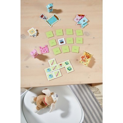 Jogo de cartas e peças coloridas sobre mesa de madeira clara com cão de peluche num cadeirão branco