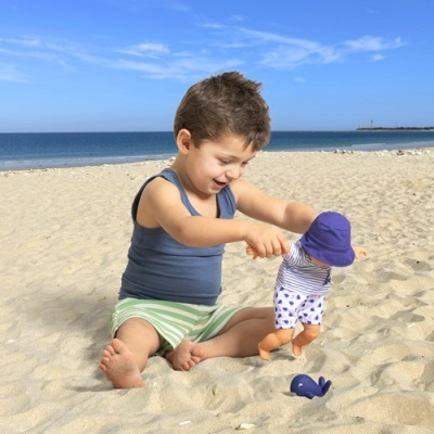 Criança na praia a brincar com boneca vestida com chapéu roxo