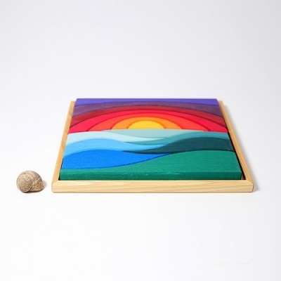Jogo de madeira colorido em moldura quadrada com padrão de pôr do sol e ondas, ao lado uma concha marinha.