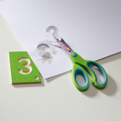 Tesouras verdes com interior azul ao cortar papel branco próximo a stencil verde com número 3