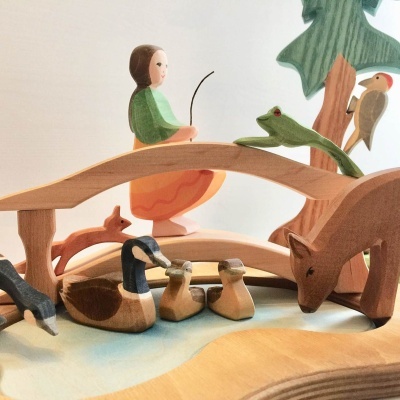 Figura de madeira com pessoa e animais junto a ponte sobre água.