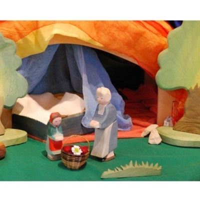 Miniatura de figuras em madeira pintada num cenário pastoral colorido com tecido e árvores de madeira.