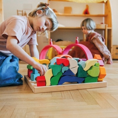 Crianças a brincar com blocos de madeira coloridos num ambiente interior com prateleiras de madeira