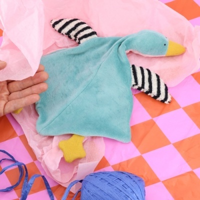 Boneco de peluche em forma de pato azul com asas listradas e bico amarelo