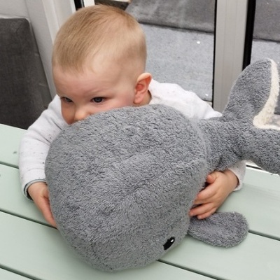 Bebé abraçando uma pelúcia de baleia cinzenta sobre uma mesa verde clara