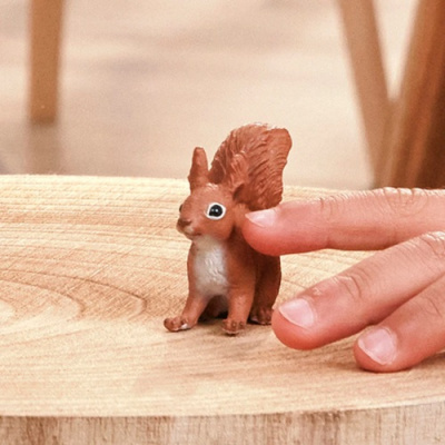 Miniatura de esquilo castanho e branco sobre madeira com dedos ao lado