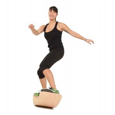 Prancha de equilíbrio de madeira clara com base curva e plataforma preta usada por mulher em fundo branco.