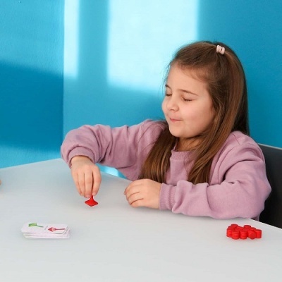 Criança a jogar com cartas e fichas vermelhas numa mesa branca