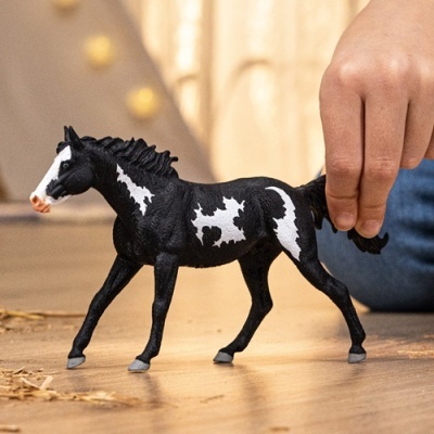 Figurinha de cavalo preto e branco num chão de madeira com mão infantil a segurá-la