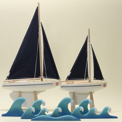 Modelos de barcos à vela com velas pretas sobre suportes em forma de ondas azuis