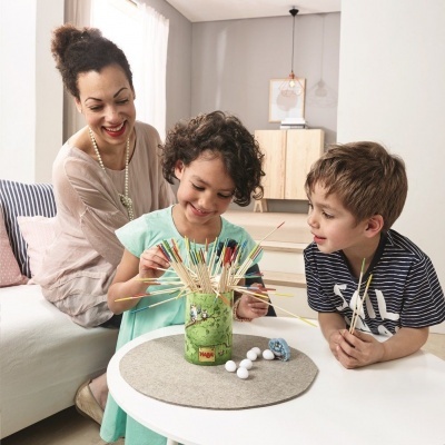 Crianças e mulher a jogar jogo de palitos coloridos numa mesa branca interior