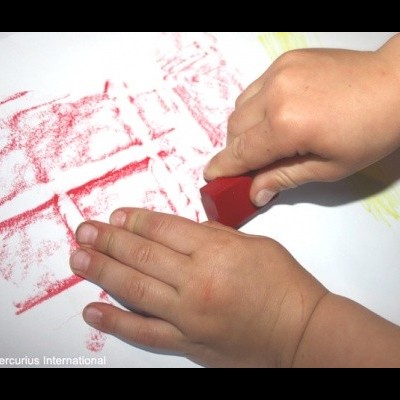 Criança a desenhar com lápis de cera vermelho sobre papel branco