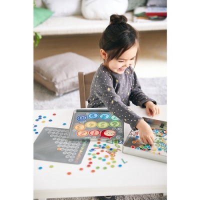 Criança a jogar jogo educativo com fichas coloridas e tabuleiros em mesa branca