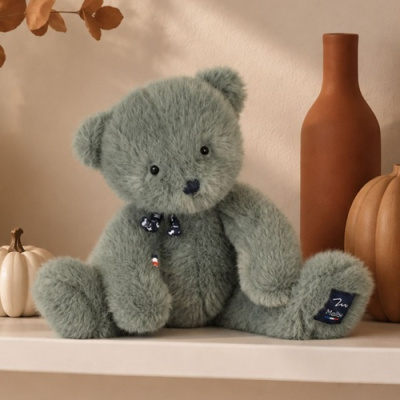 Ursinho de peluche cinza com laço azul escuro sentado numa prateleira com decoração