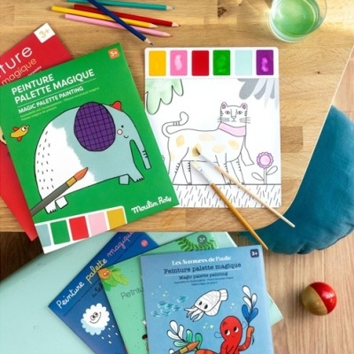 Livros de pintura mágica para crianças com paletas de cores e temas de animais numa mesa de madeira