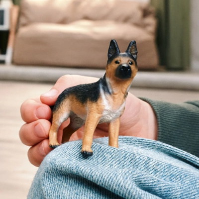Miniatura de cão pastor alemão em plástico colorido sobre joelho de ganga
