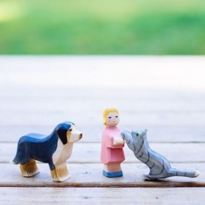 Figuras em madeira pintada de cão, menina e gato sobre chão de madeira.