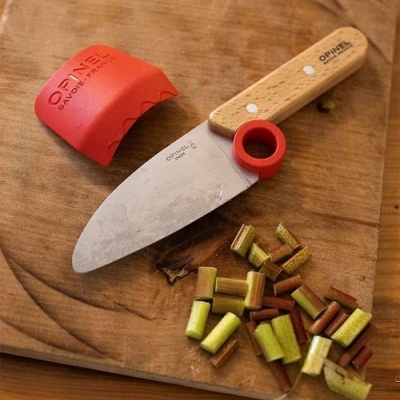 Faca de cozinha OPINEL com cabo de madeira e protetor vermelho numa tábua de cortar com pedaços de legumes