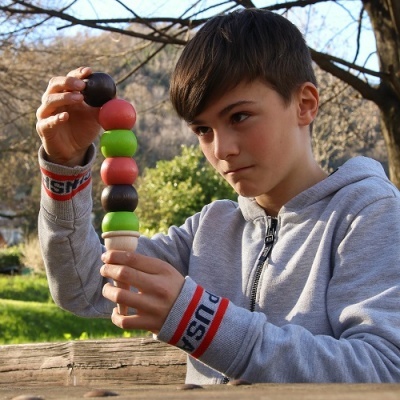 Adolescente a empilhar bolas de madeira coloridas ao ar livre