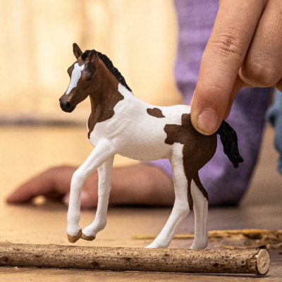 Brinquedo de cavalo castanho e branco sendo segurado por uma mão sobre madeira