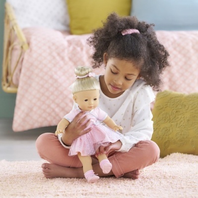 Menina sentada segurando boneca vestida de rosa num ambiente acolhedor.
