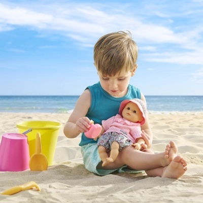 Criança a brincar na praia com boneca e brinquedos coloridos na areia