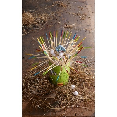 Garrafa verde com palitos coloridos e ovos num ninho de palha sobre madeira