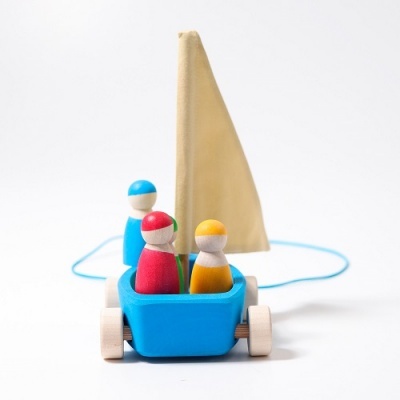 Brinquedo barco azul de madeira com três bonecos coloridos e vela bege