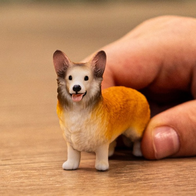 Miniatura de cão Corgi pintada em tons castanhos e brancos, com textura de pêlo e mão ao fundo