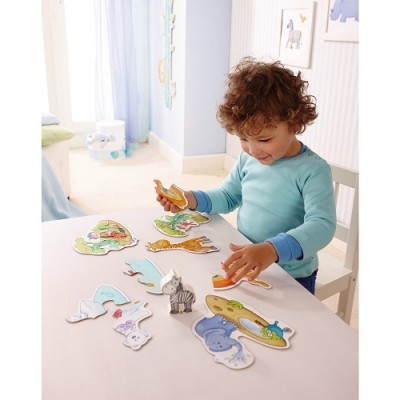 Criança a brincar com puzzles de animais de madeira numa mesa branca num quarto claro.