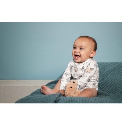 Bebé vestido com body estampado e segurando peluche sentado sobre manta azul.