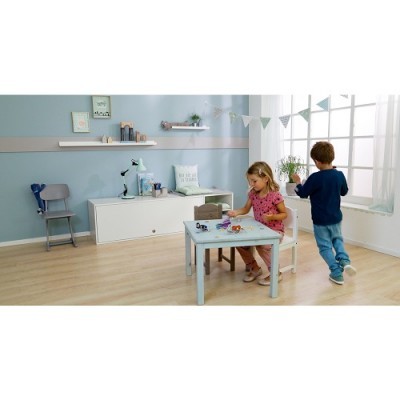 Mesa infantil azul clara com cadeira branca e duas crianças num quarto com parede azul e móveis brancos