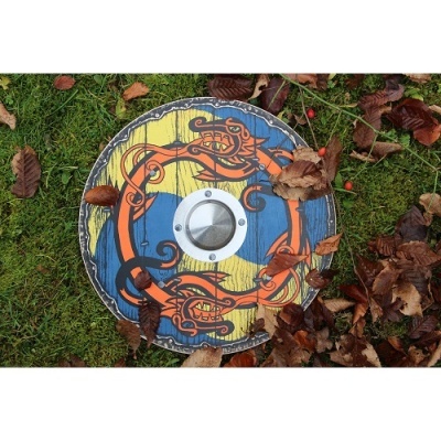 Escudo circular azul, amarelo e laranja com centro metálico sobre relvado com folhas secas