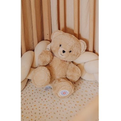 Ursinho de peluche castanho claro dentro de berço com almofadas brancas entrelaçadas