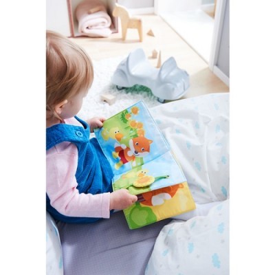 Criança com vestido azul a ler livro infantil colorido numa cama com roupa de cama branca com padrões azuis e roxos
