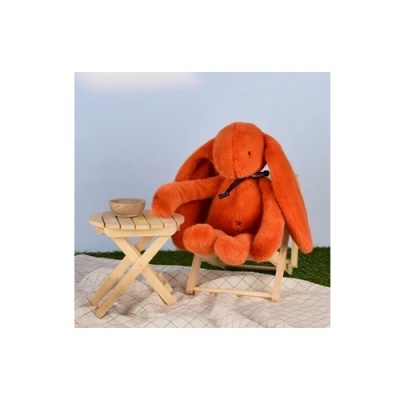 Coelho de peluche laranja numa cadeira de madeira ao lado de mesa pequena com tigela