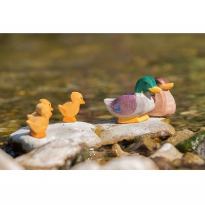 Figuras decorativas de patos coloridos colocadas sobre pedras em água rasa.