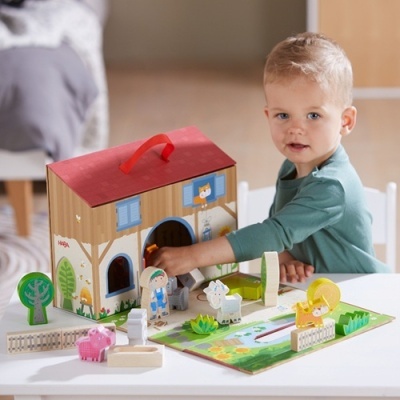 Brinquedo infantil de madeira temática de quinta com animais e casa, criança a brincar numa mesa branca