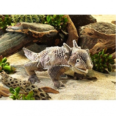 Figura de dinossauro tecido com padrão escamoso em fundo de areia e plantas