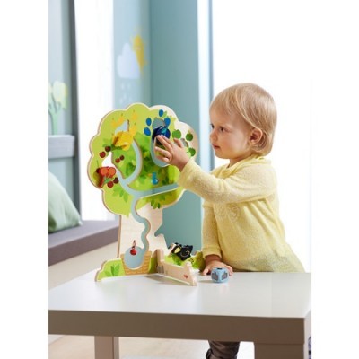 Criança a brincar com brinquedo de madeira colorido em forma de árvore numa mesa branca