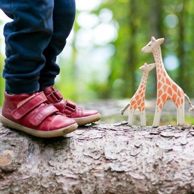 Criança com sapatos vermelhos e duas figuras de girafas em tronco de árvore ao ar livre