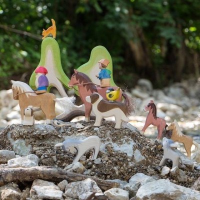 Brinquedo de madeira com cavalos e figuras humanas em ambiente natural rochoso