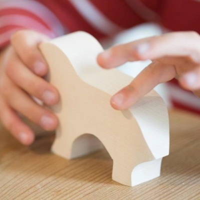 Figura de elefante em madeira clara nas mãos de uma criança sobre mesa de madeira