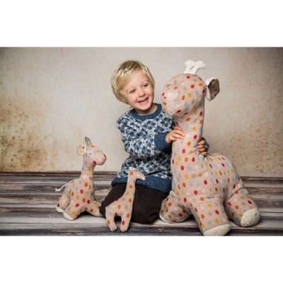 Três peluches de girafa com bolinhas coloridas e criança sorridente em fundo neutro