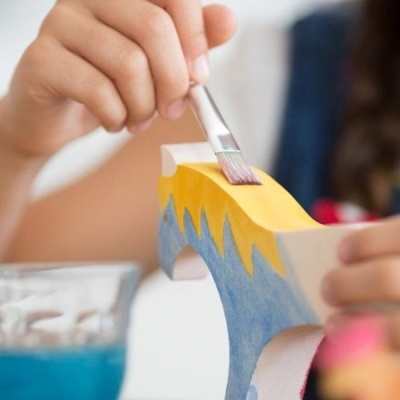 Pessoa a pintar suporte de madeira branco com tinta amarela e azul com pincel fino