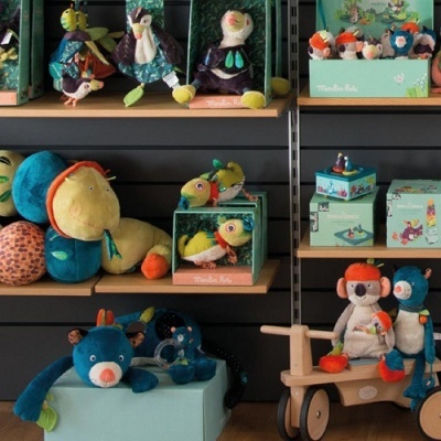 Brinquedos de pelúcia coloridos e caixas verdes com texto Moulin Roty em prateleira cinzenta